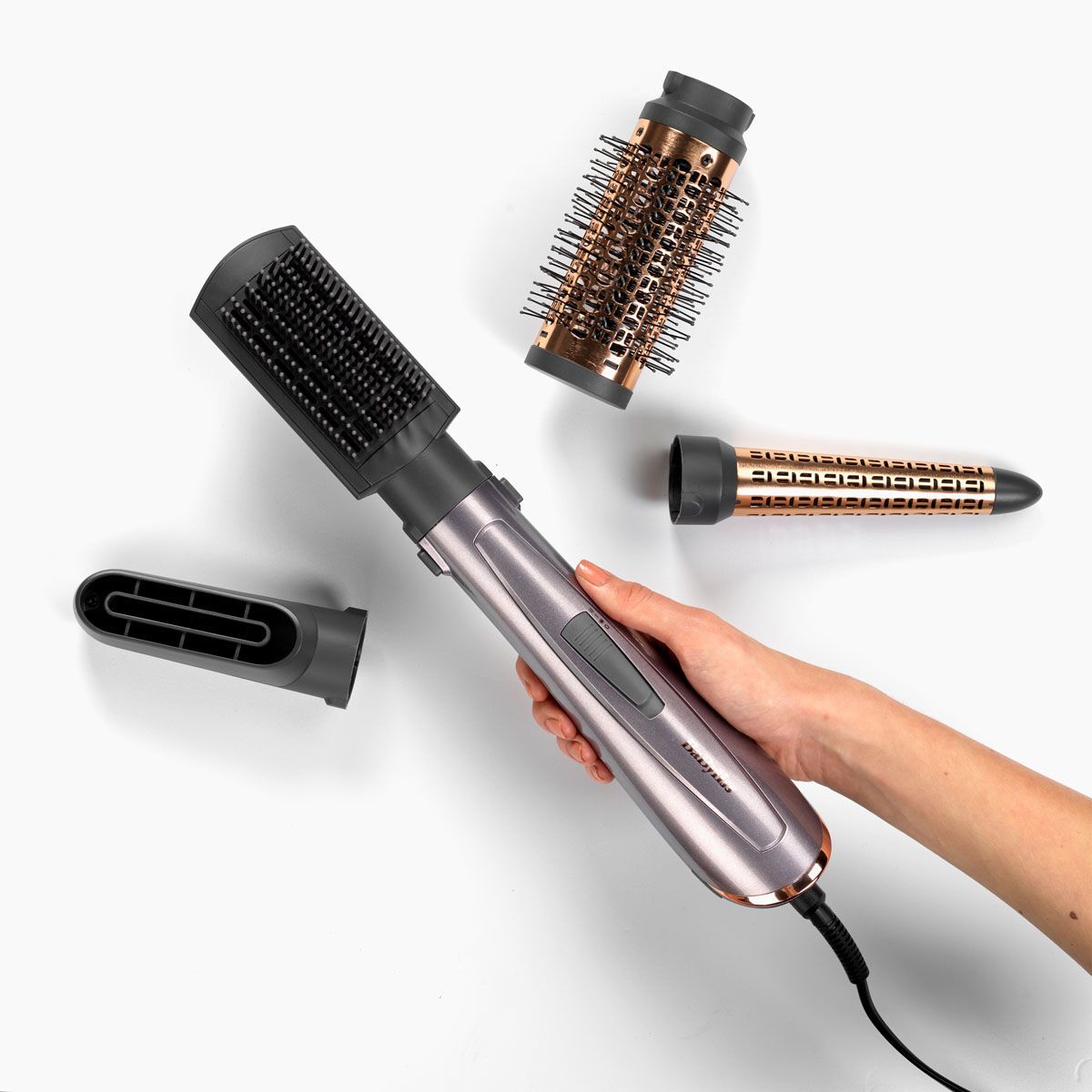 Air Style 1000 in hand with paddle brush attached, with 3 attachments (drying nozzle, thermal brush, conical curler) around it